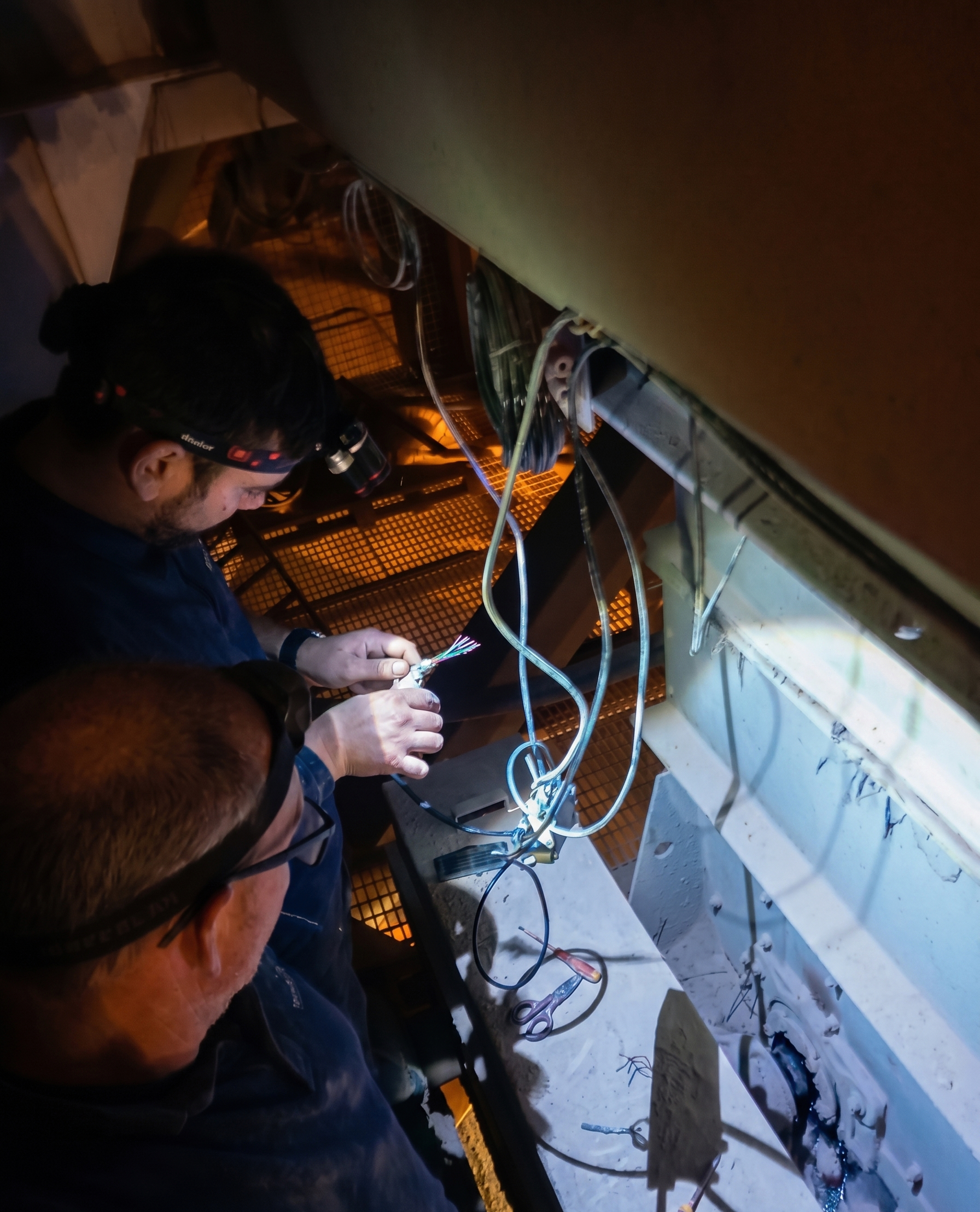 Dos técnicos de TecniPés con linternas frontales conectando cableado en un cuadro eléctrico durante una intervención nocturna.