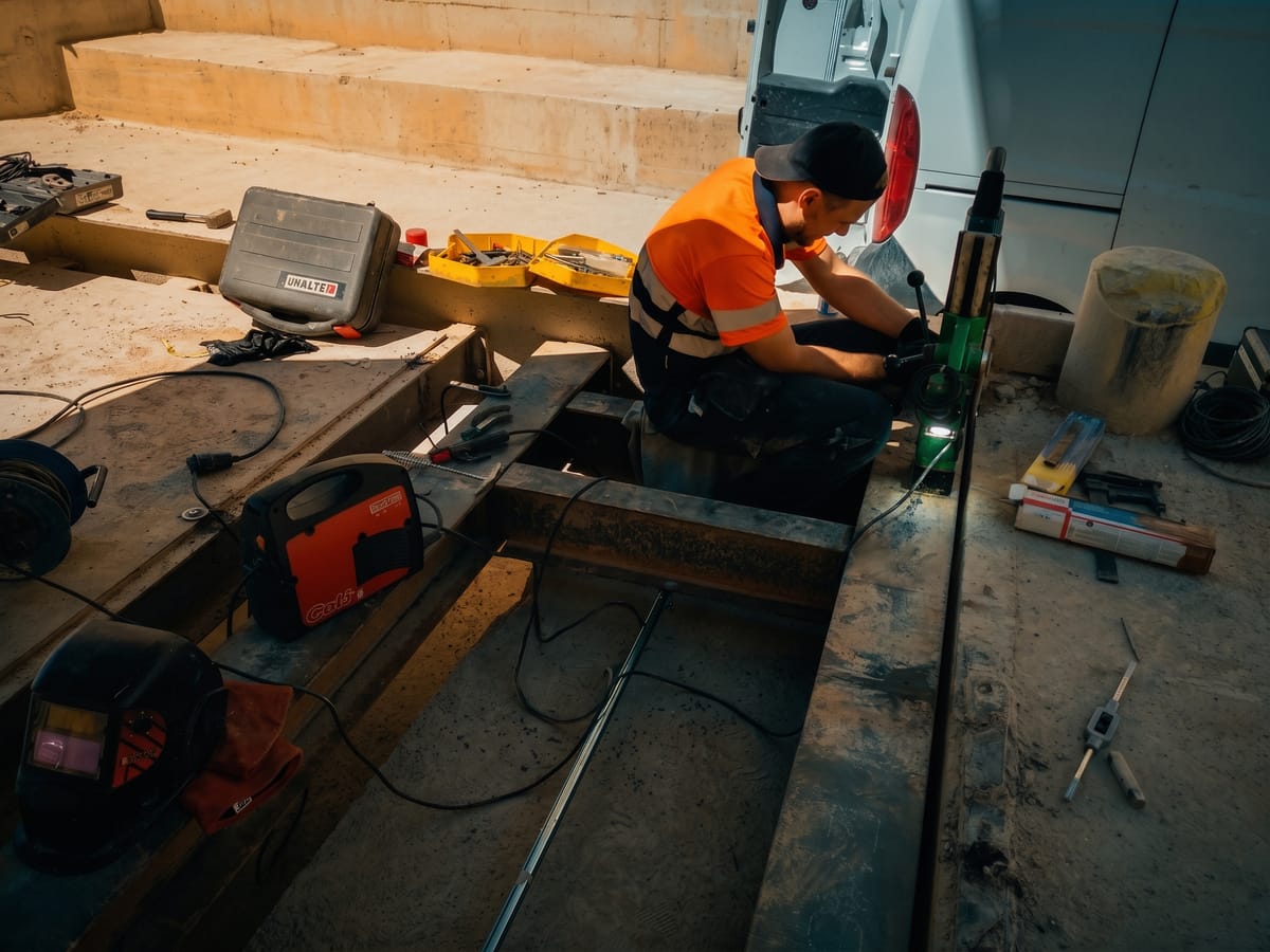 Técnico de TecniPés con chaleco fluorescente trabajando sobre una báscula puente para camiones enrasada en el suelo, con herramientas y soldadora alrededor.